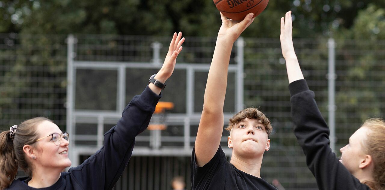 drei Jugendliche spielen zusammen Basketball