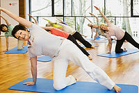 Eine fröhliche Damengruppe macht Yoga in einem Gymnastikraum auf blauen Bodenmatten.